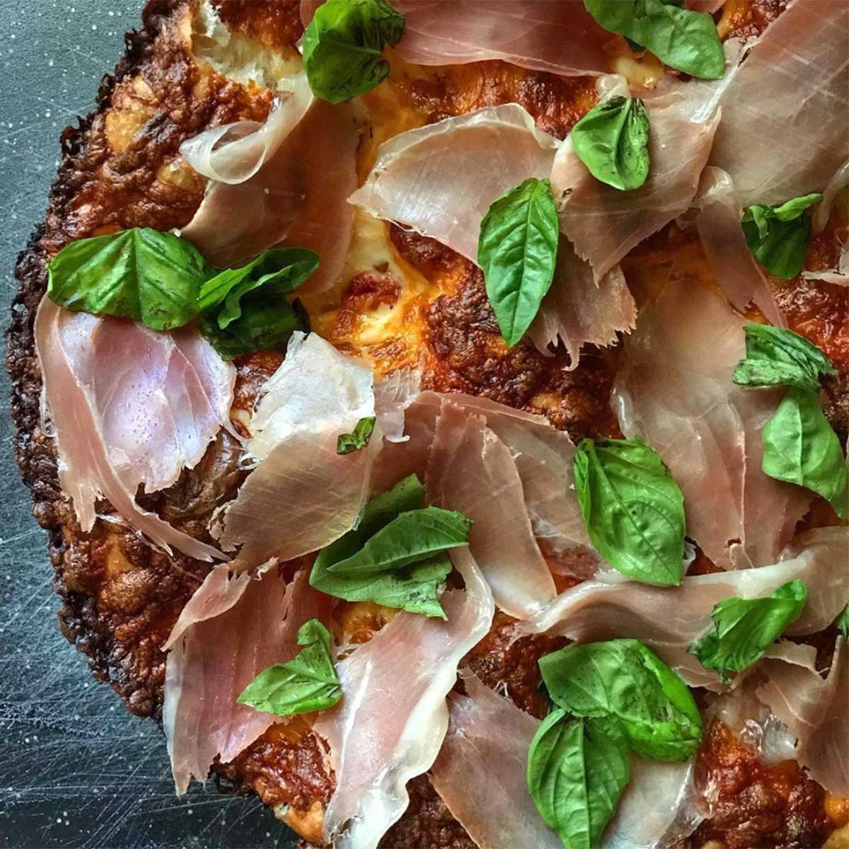 Pizza topped with basil and prosciutto