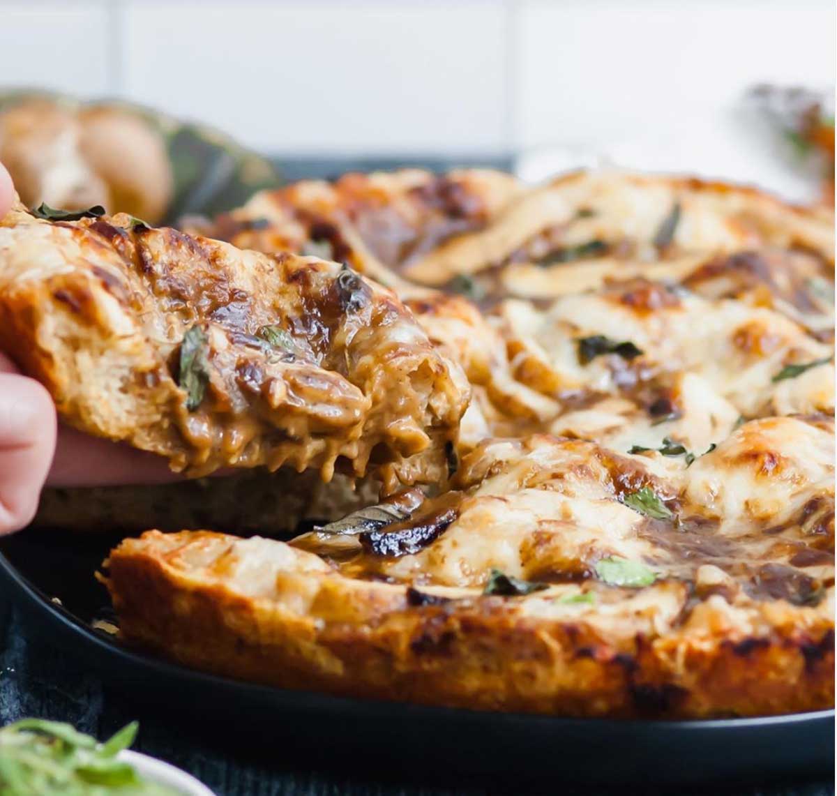 Hand pulling slice from baked pizza