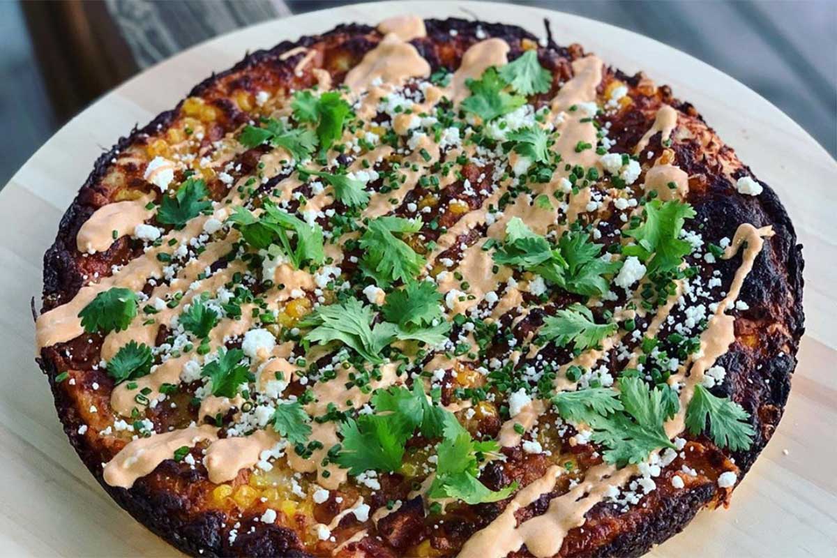 Round plated pizza with artfully drizzled sauce and cilantro