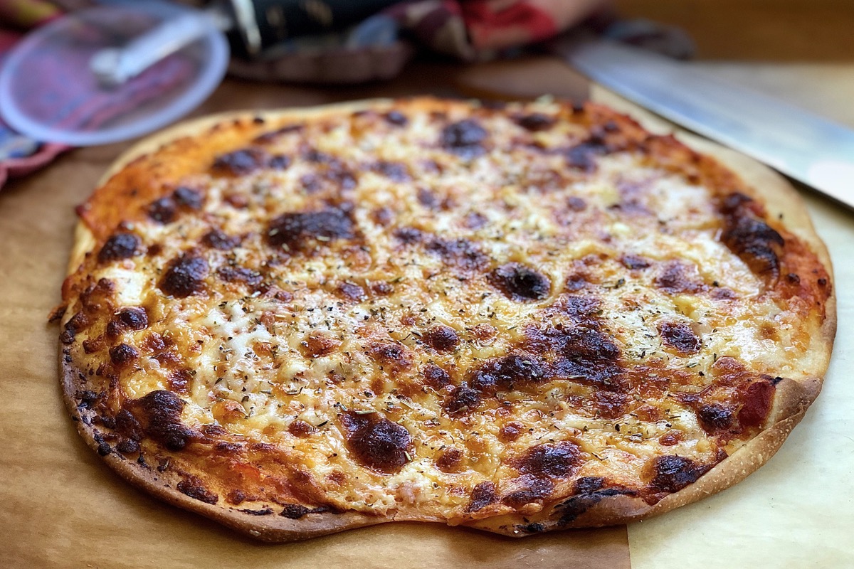 An oval thin-crust cheese pizza on a cutting board, ready to be cut up and served.