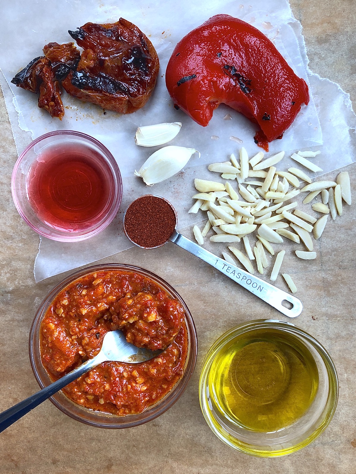 Ingredients for romesco sauce, including roasted red bell pepper, oven-roasted tomatoes, red wine vinegar, garlic cloves, slivered almonds, smoked paprika, and olive oil