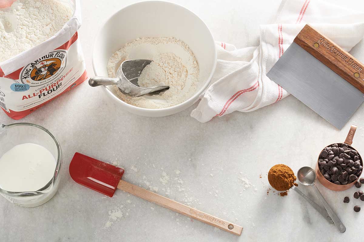 A bag of flour and a measuring cup of chocolate chips on a kitchen table