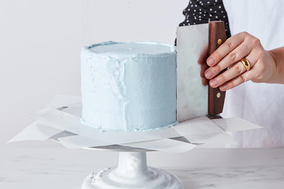 Using bench knife to smooth frosting on cake sides