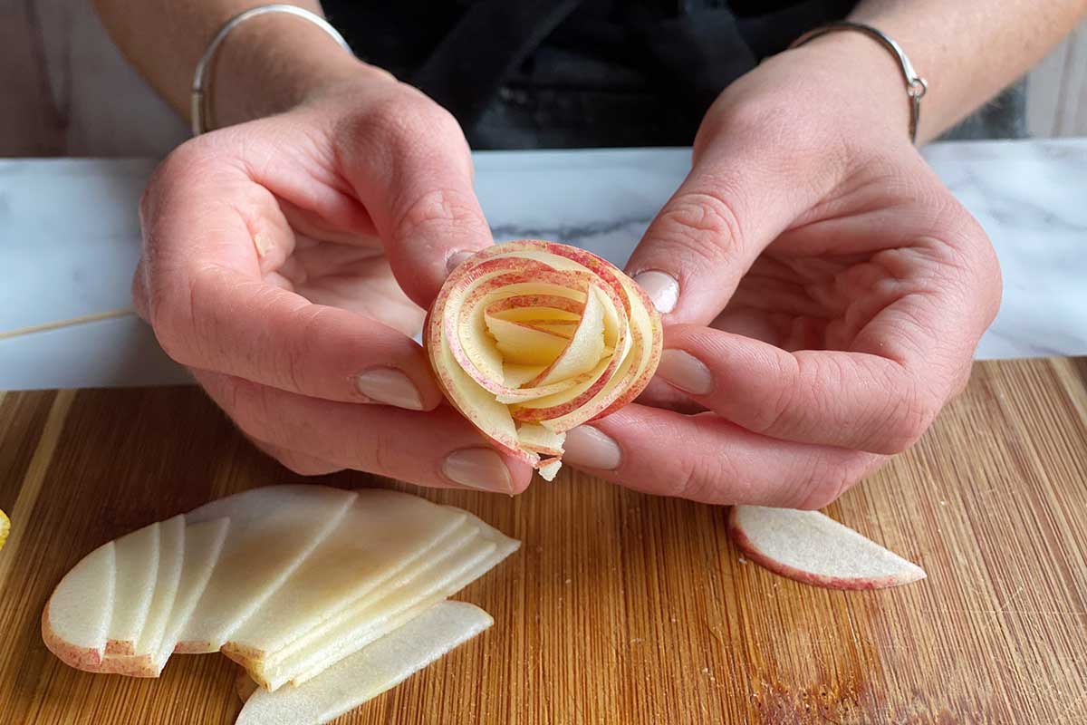 A baker's hands showing the center of the rose apple pie to the camera