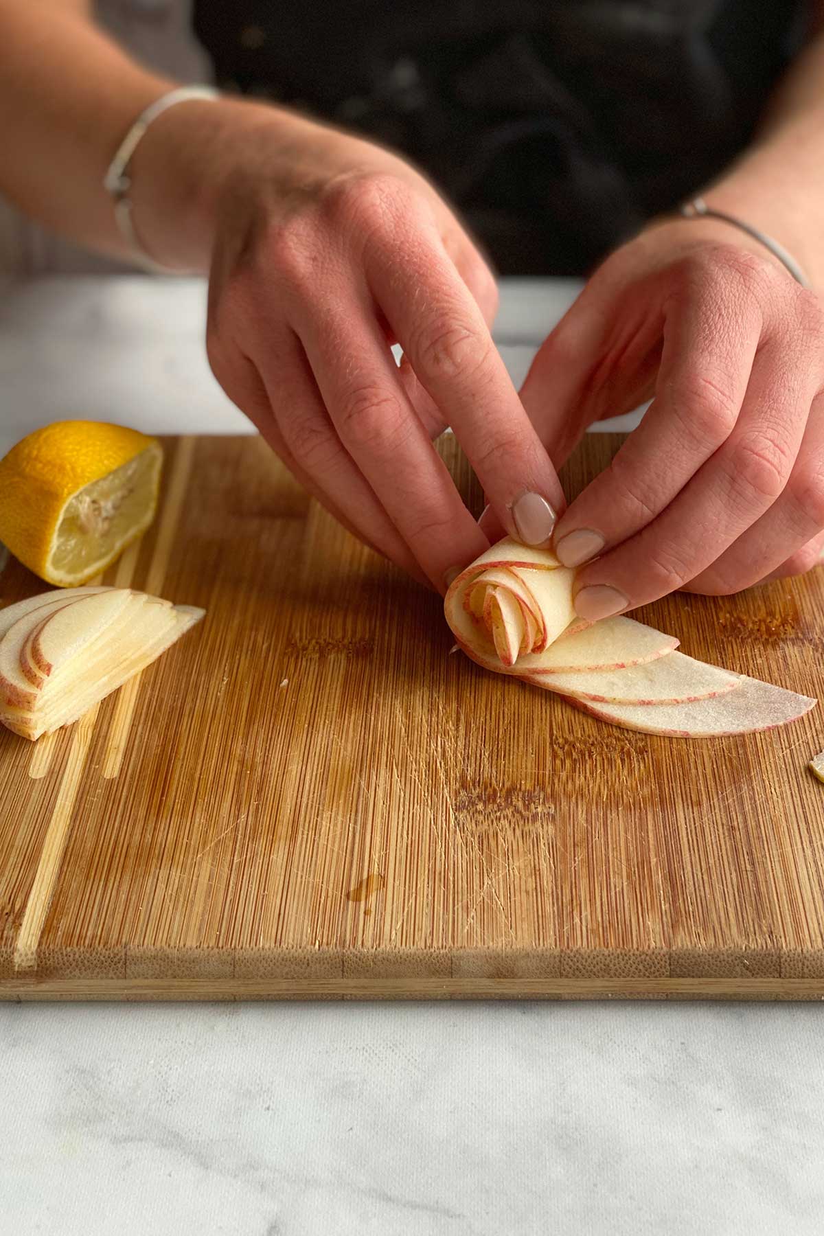 A baker rolling up slices of apple to make the center of a rose apple pie