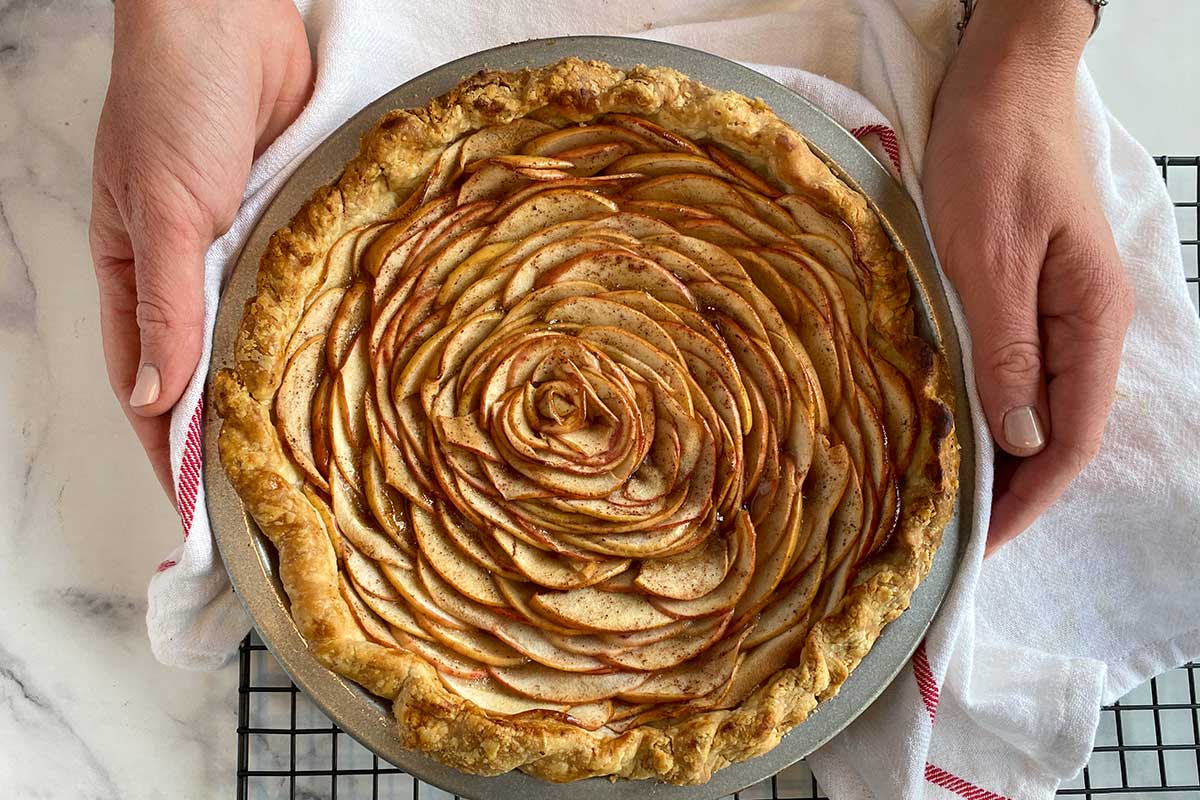 A baker's hands placing a freshly baked rose apple pie on a cooling rack
