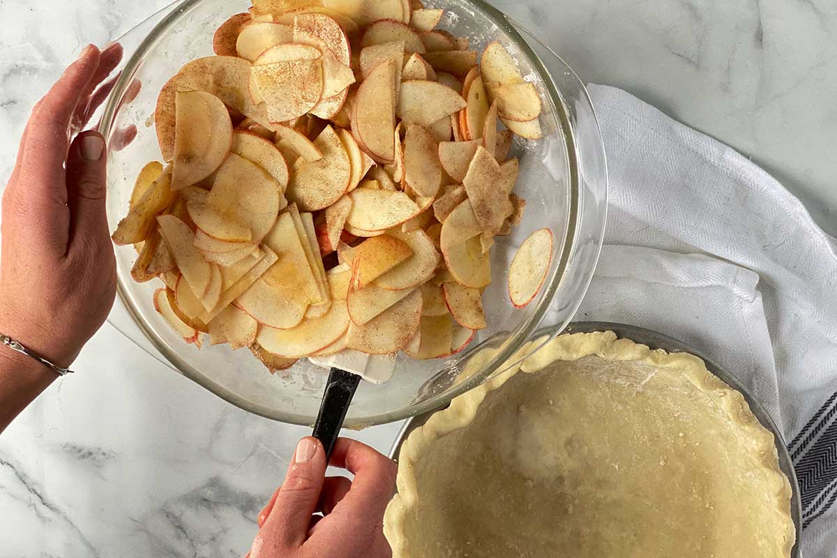 A baker mixing a bowl of apple slices with cinnamon and sugar