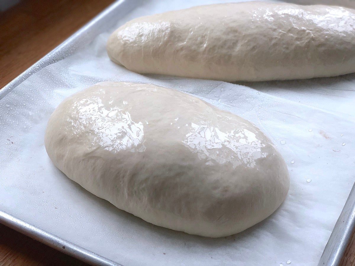 Risen loaf of sourdough bread sprayed with water.