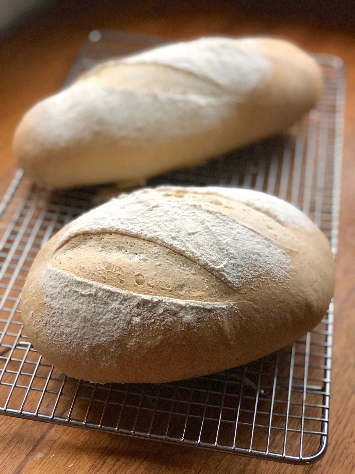 Two loaves of baked sourdough bread on a cooling rack.