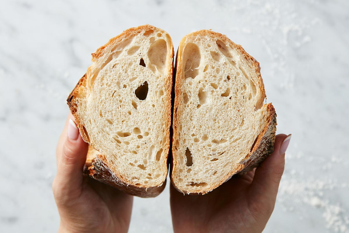 A loaf of sourdough bread cut in half, with a baker exposing the crumb