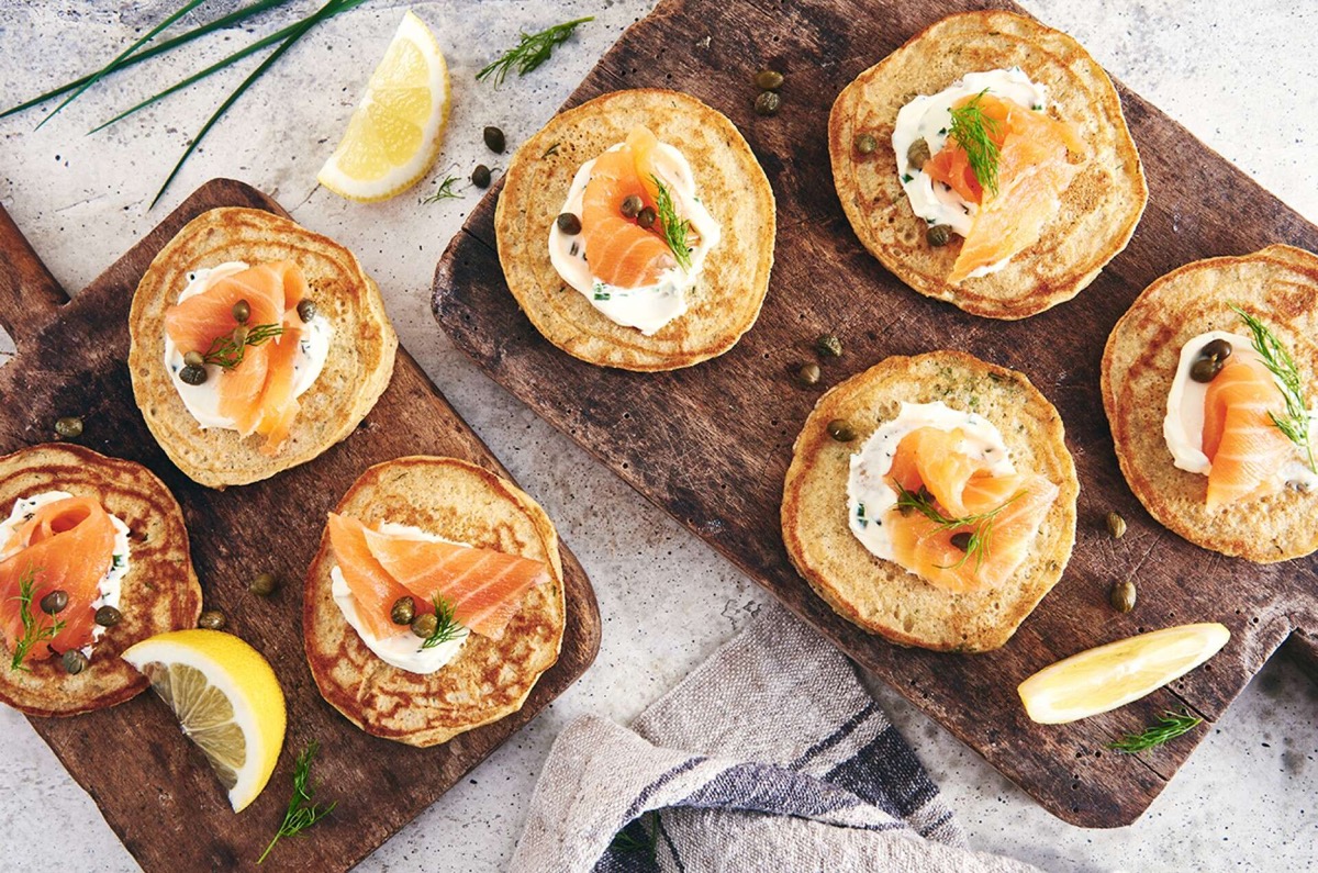 Appetizer rye pancakes topped with sour cream and smoked salmon on a serving board