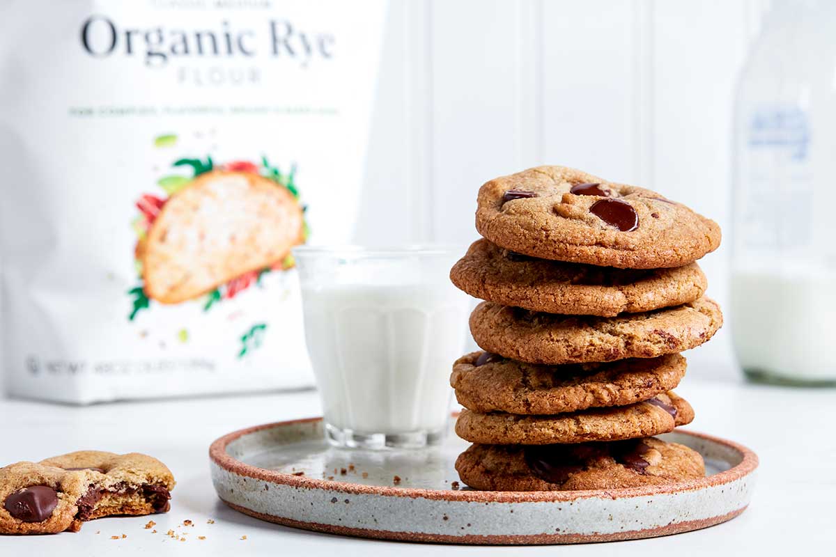 A stack of rye chocolate chip cookies on a plate next to a glass of milk