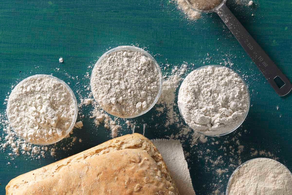 Several small bowls of various rye flours, next to a loaf of rye bread