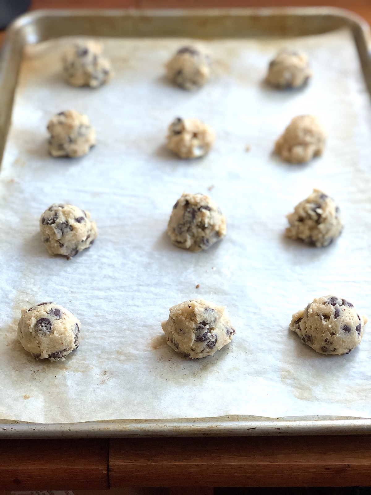 Scooped-out balls of cookie dough spaced on a parchment-lined baking sheet.