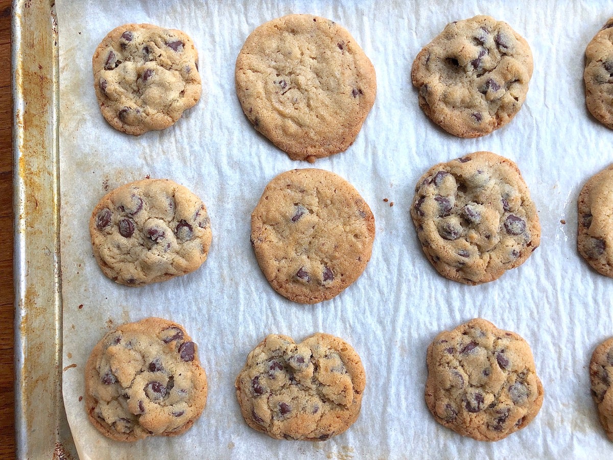 Baking sheet of baked chocolate chip cookies, including two that spread more and don't have as many chips.