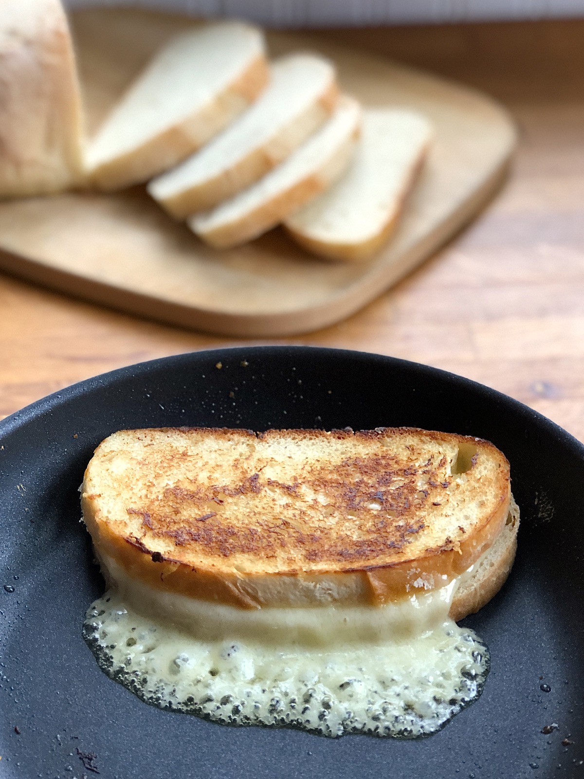 Grilled cheese sandwich in a frying pan, sliced bread in the background.