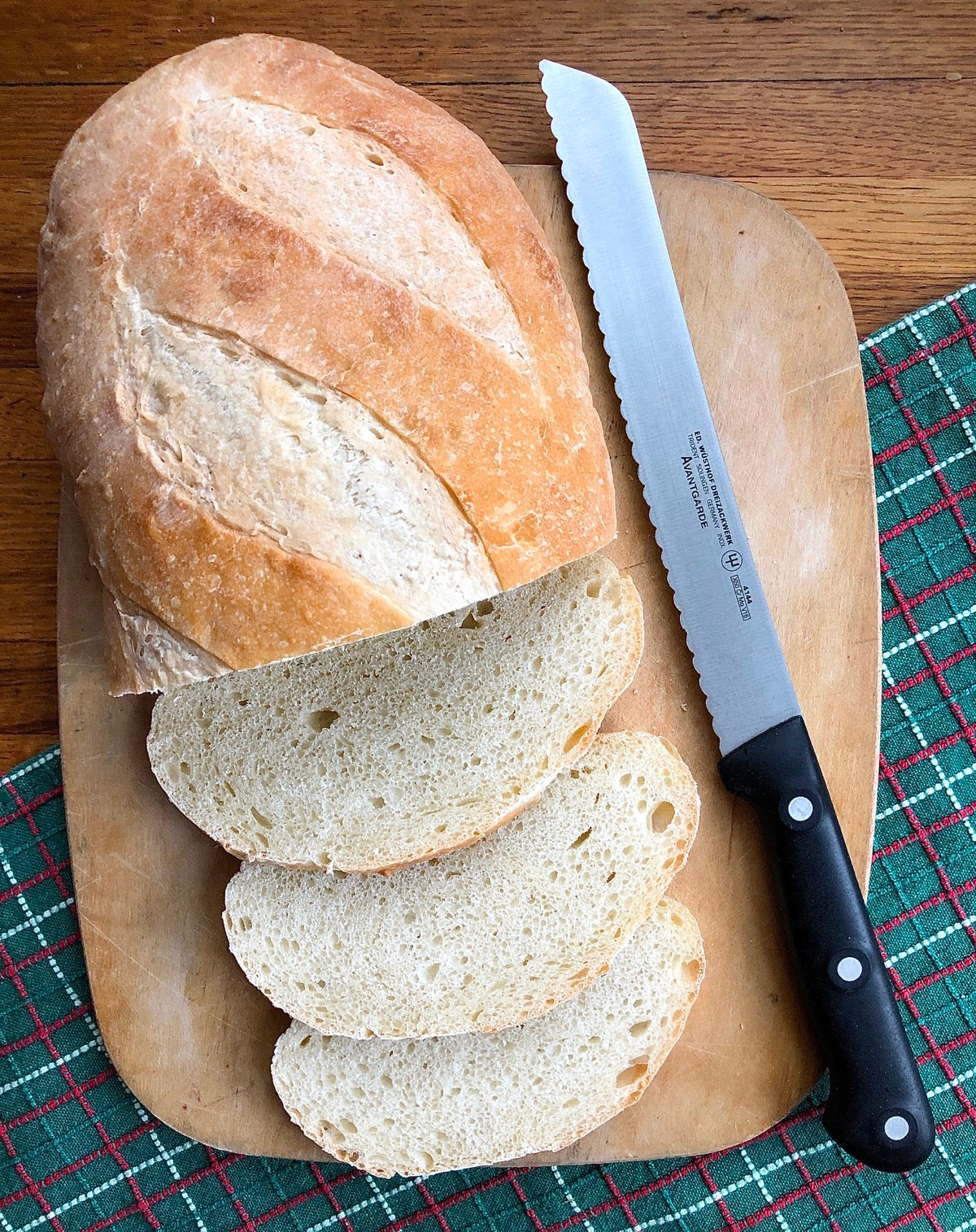 Loaf of hearth bread on a cutting board, partially sliced, serrated knife alongside.