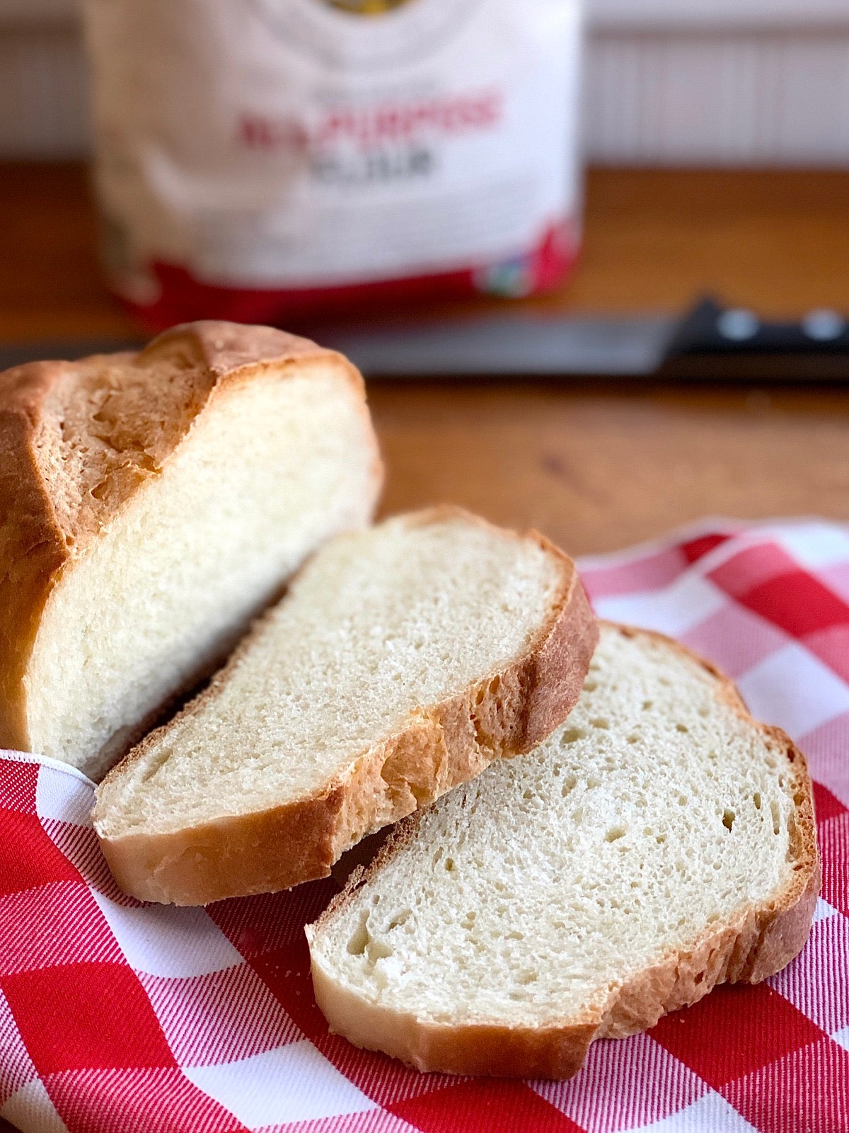 Loaf of hearth bread, partially sliced, bag of King Arthur Flour in the back.