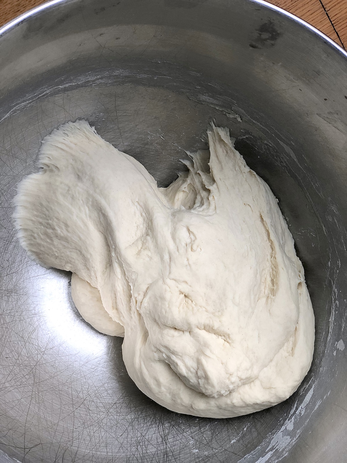 Kneaded dough in a stand mixer bowl, smooth but also barely sticking to the bottom and sides of the bowl.
