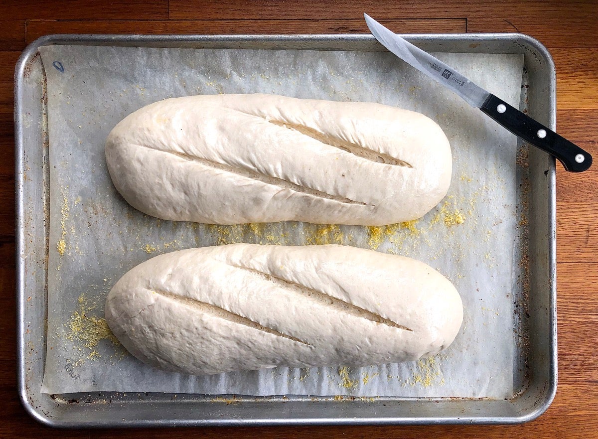 Two loaves of risen bread, each slashed diagonally three times.