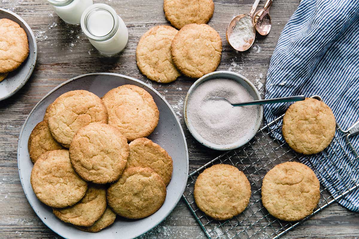 A plate of snickerdoodle cookies next to a bowl of cinnamon-sugar