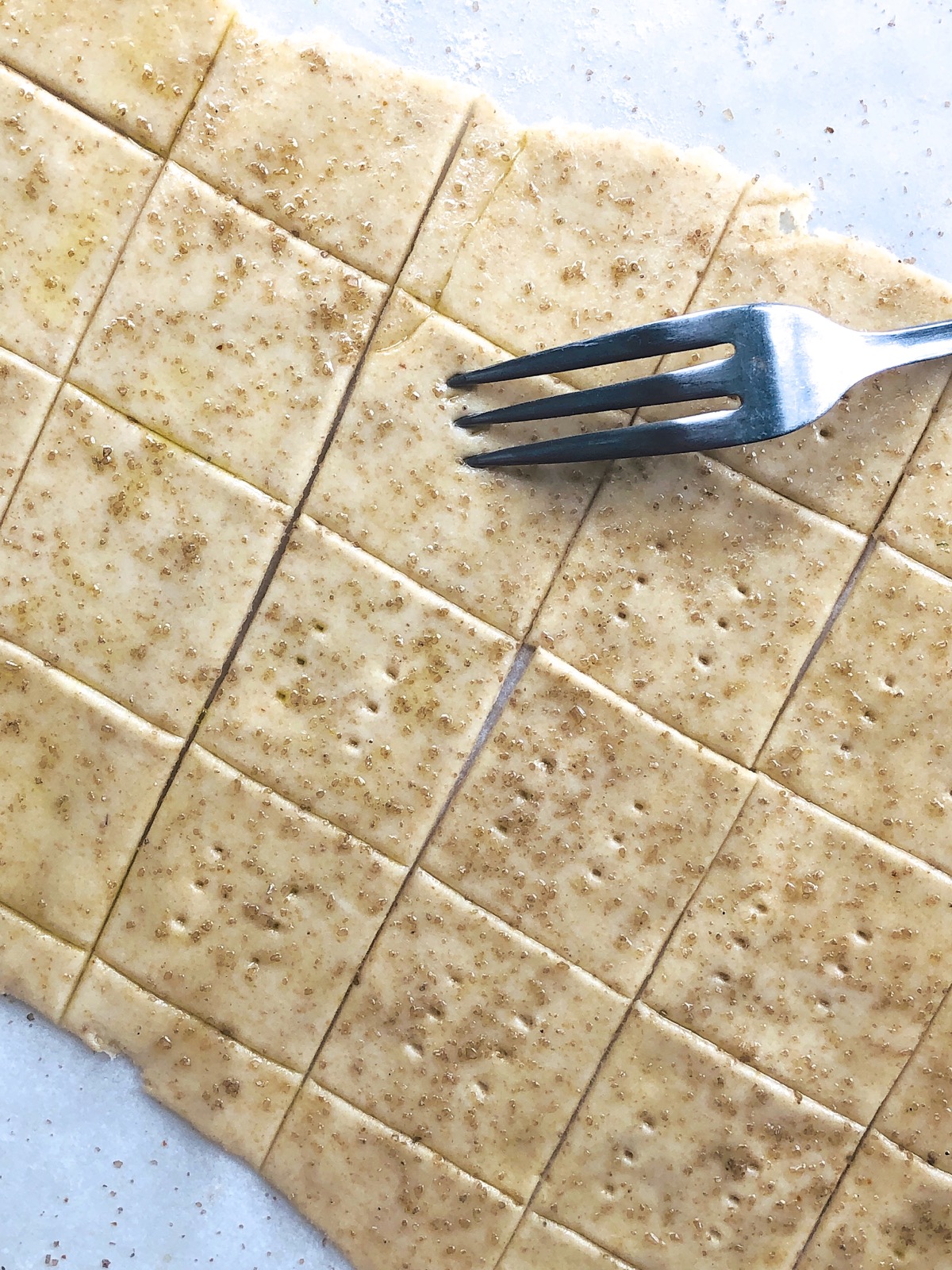 Sourdough crackers on a baking sheet being pricked with a fork prior to baking. 
