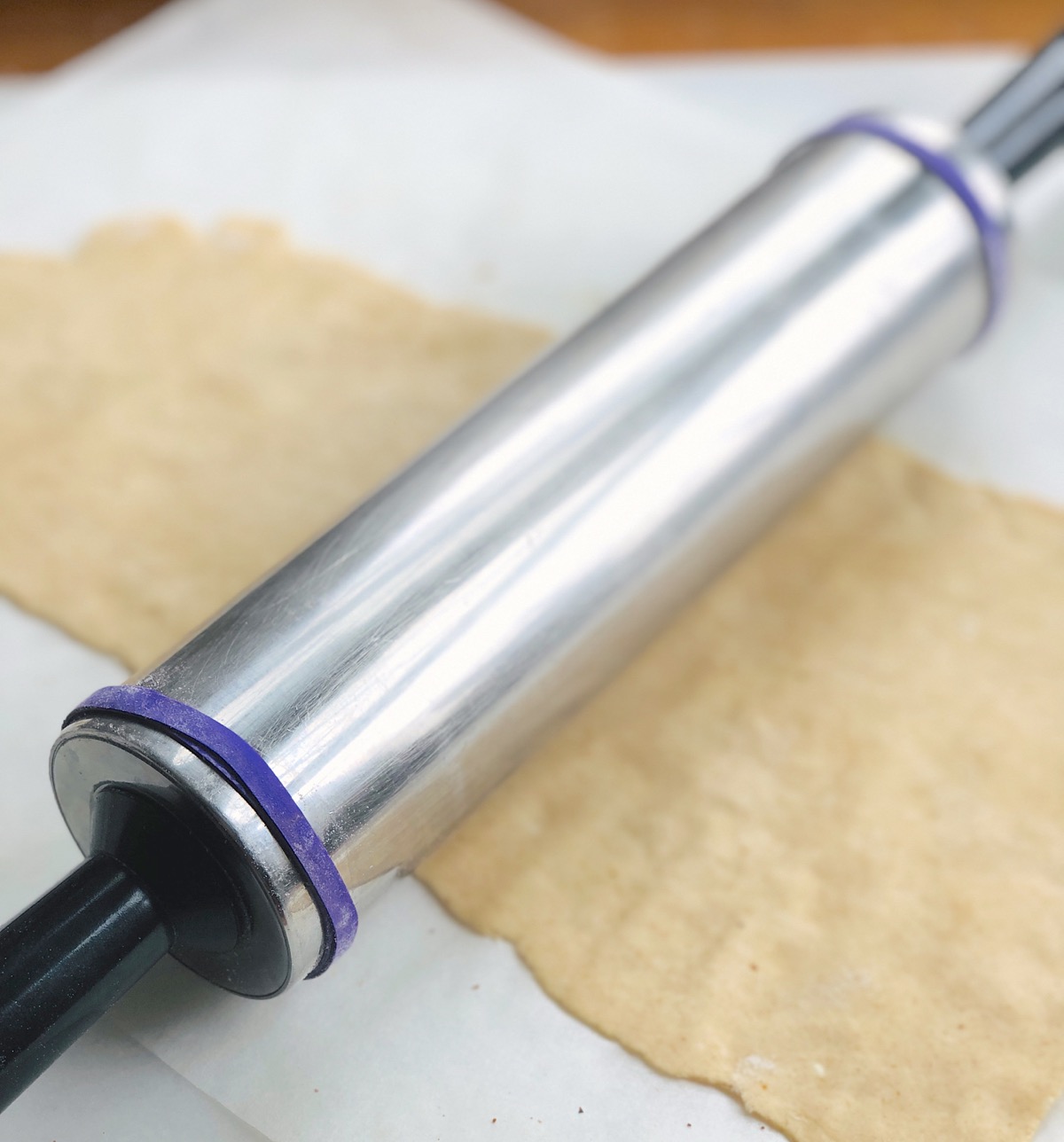 stainless steel rolling pin with two rubber bands looped at each end to create 1/16" clearance from rolling surface.
