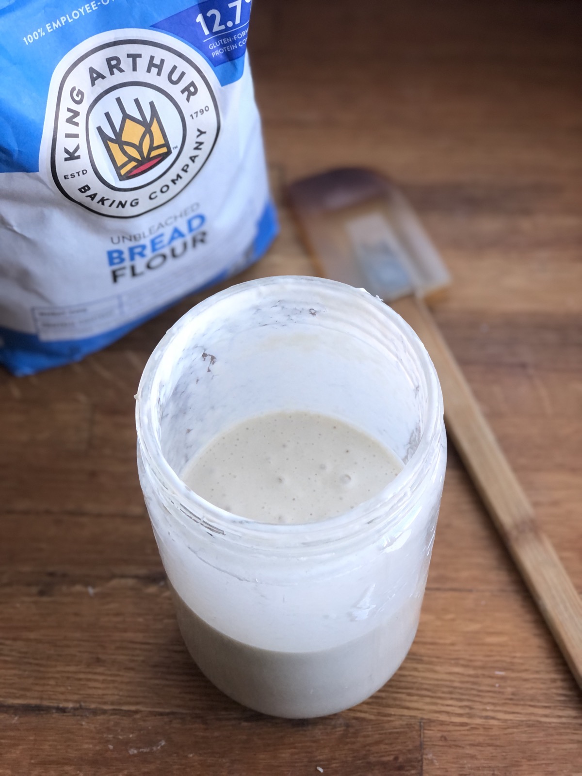 Sourdough starter in a jar, bag of bread flour and spatula in the background.