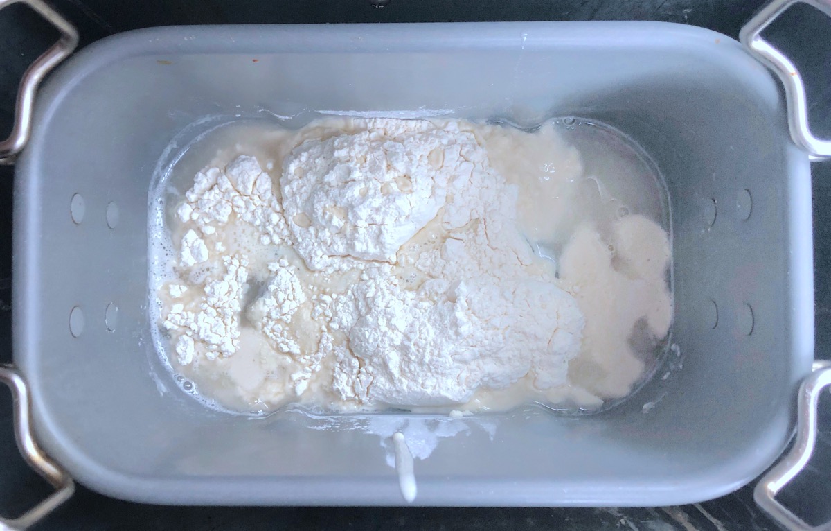 Sourdough starter in bread machine bucket being fed with flour and water 