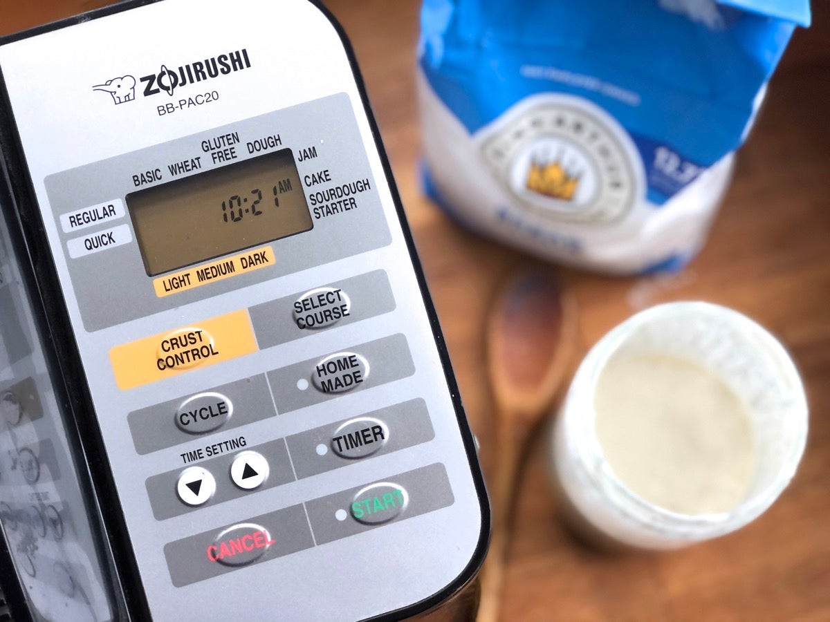 keypad of bread machine, with starter and flour in background.