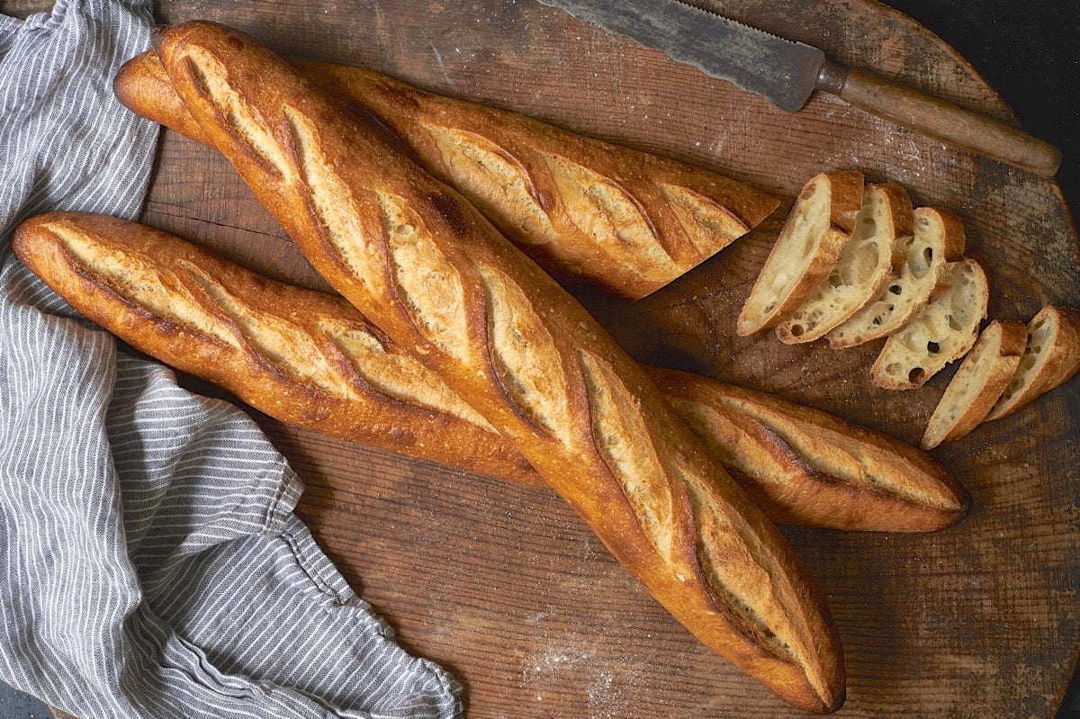 Three baguettes on a wooden table, one sliced crosswise.