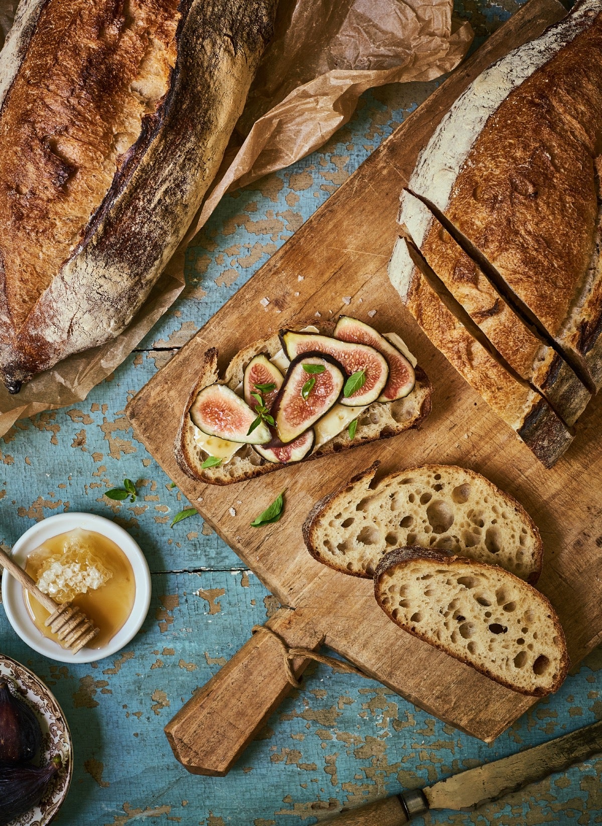 Sourdough boule on a cutting board, sliced, one slice layered with figs and cheese and drizzled with honey with