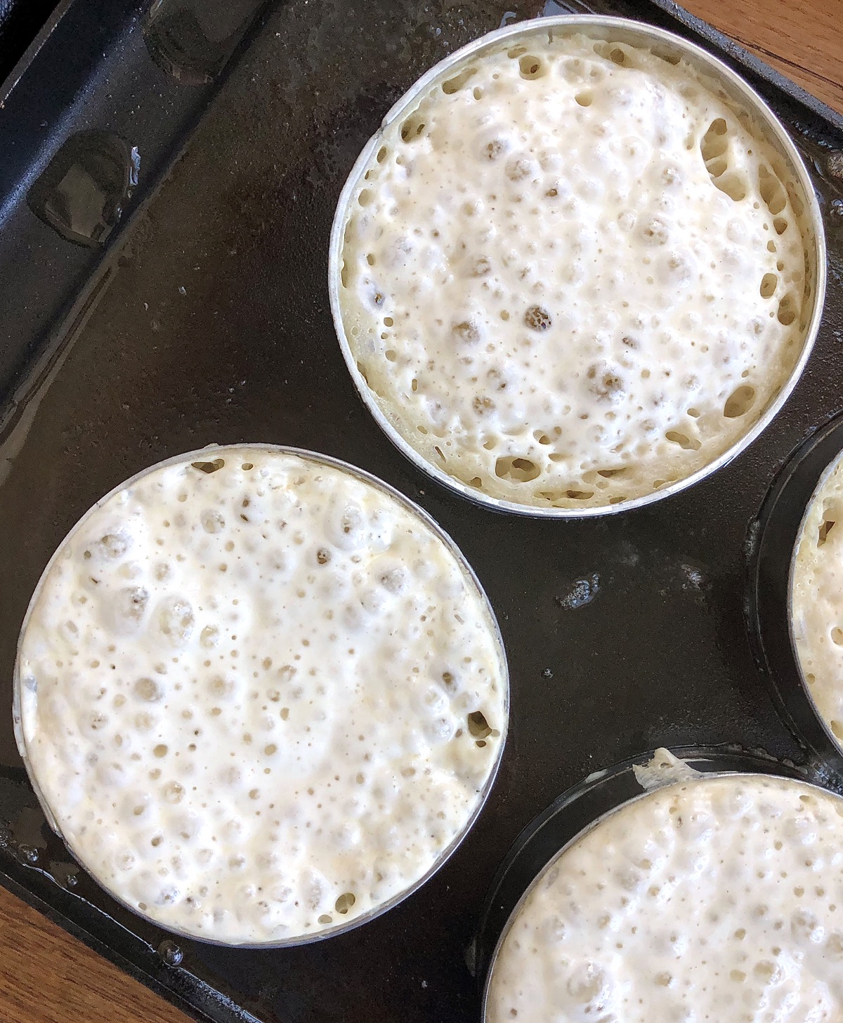 Sourdough crumpets on a griddle, ready to flip over.