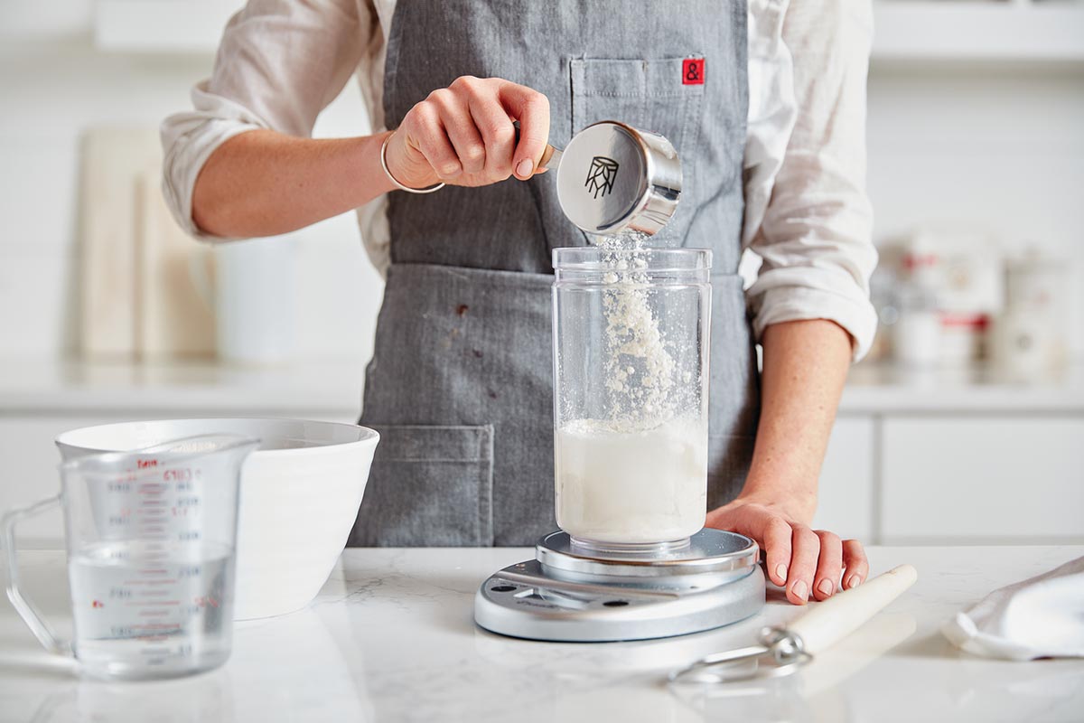 A baker adding flour to a sourdough starter