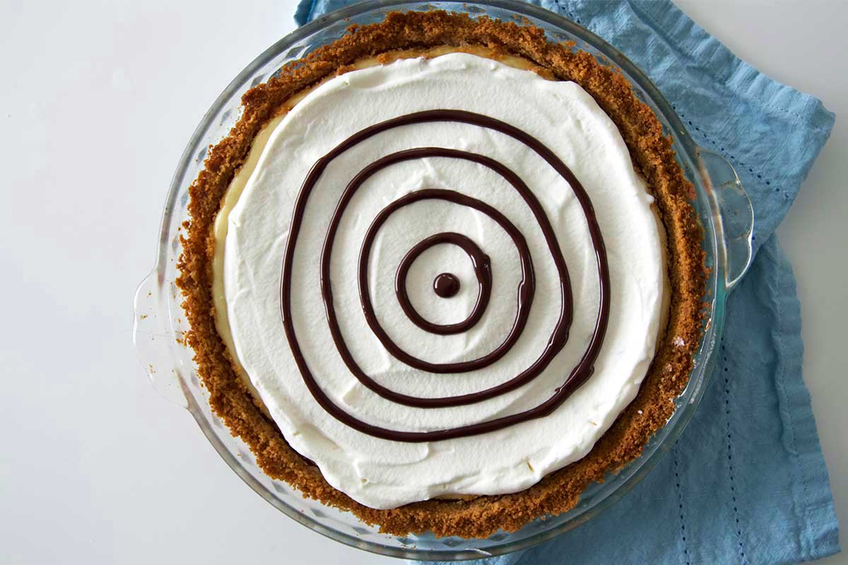 Cheesecake with four chocolate circles piped on whipped cream topping