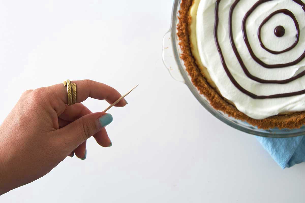 Hand holding toothpick with cheesecake in background