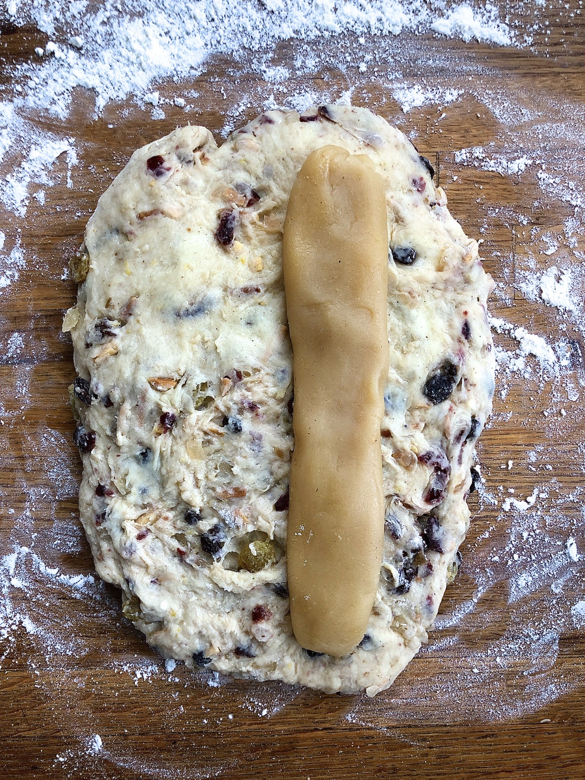 Flattened oval of stollen dough with a log of almond paste offset on top, ready to seal inside.