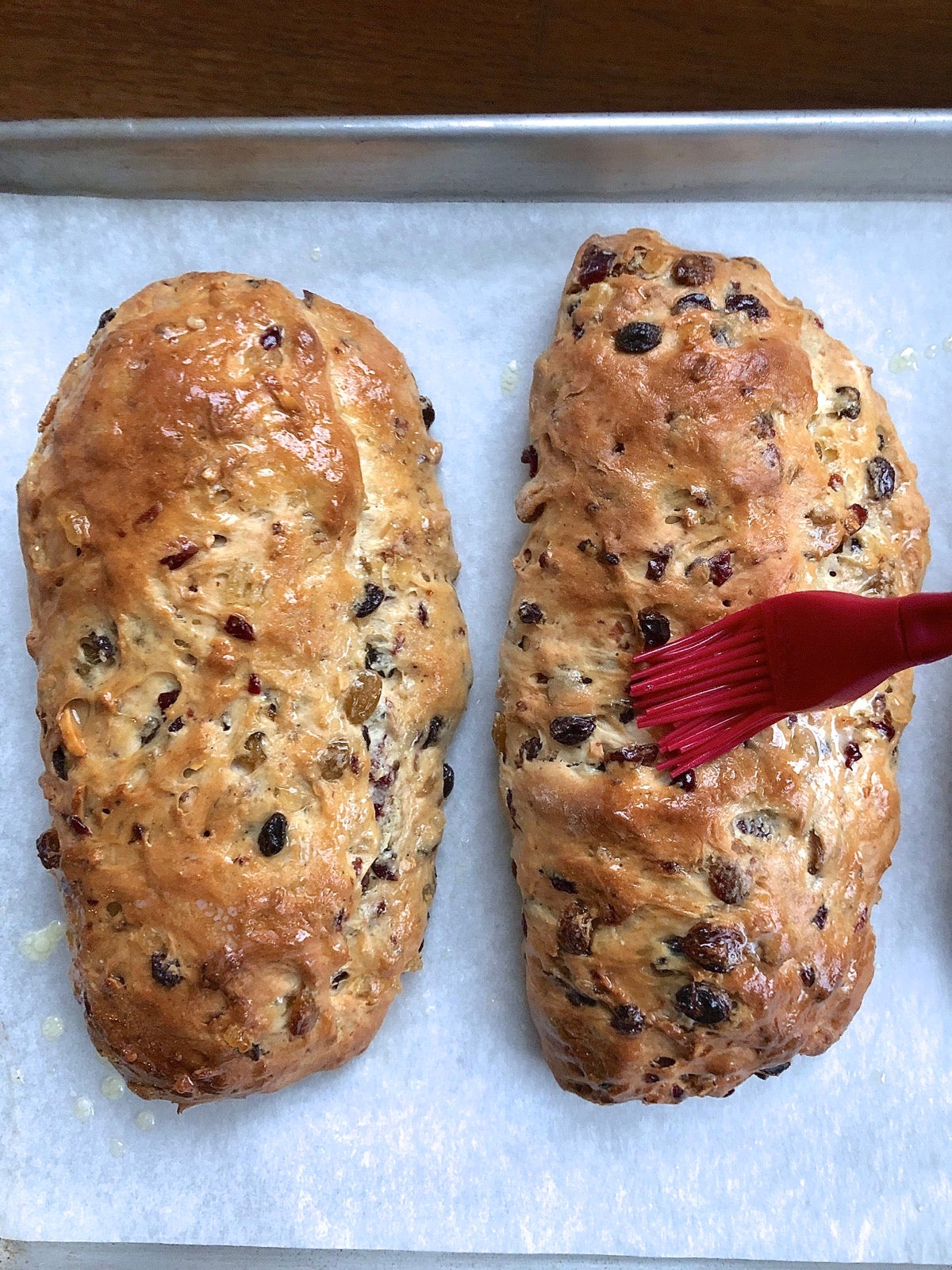 A loaf of hot stollen being brushed with melted butter.