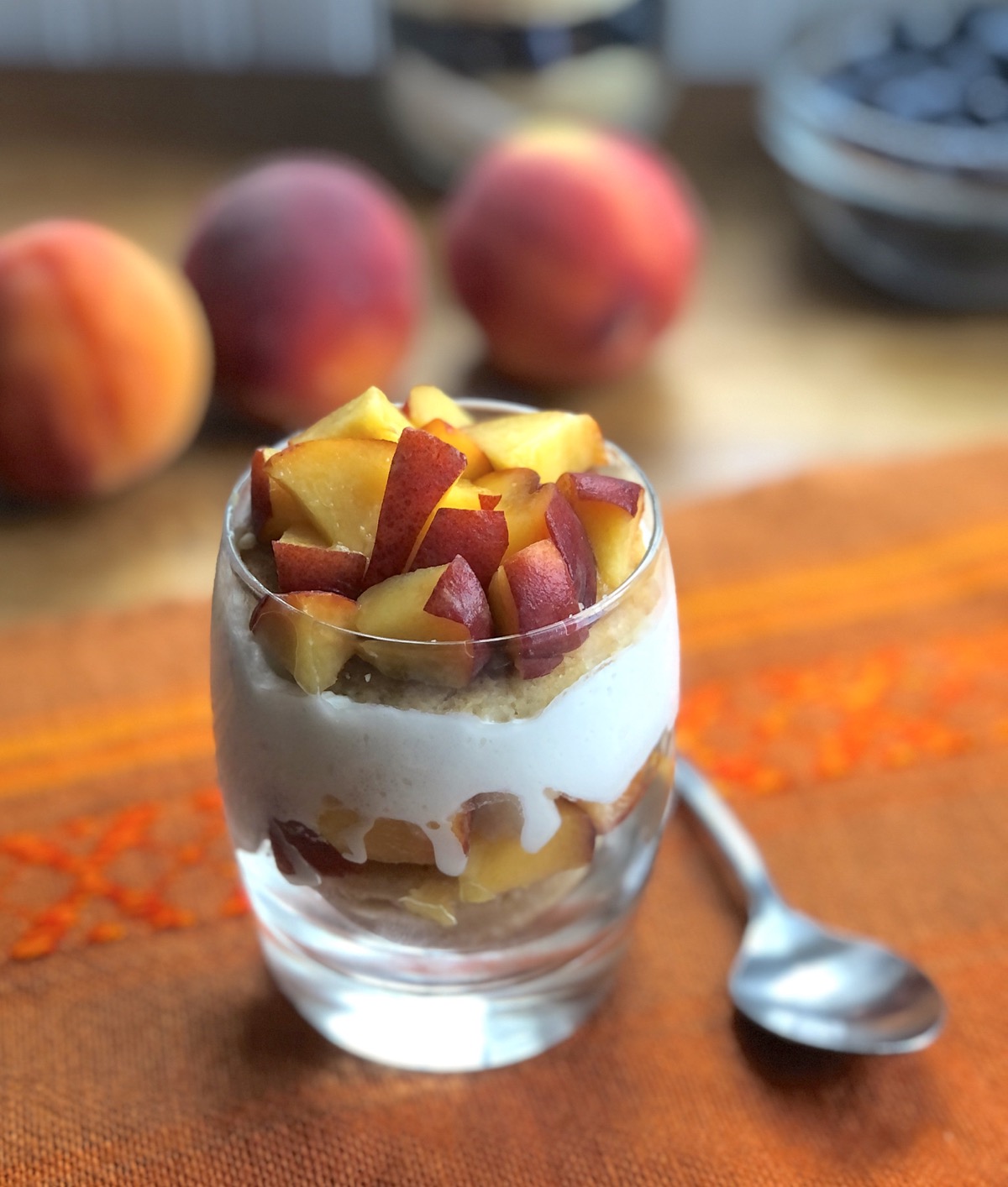A peach shortcake in a clear cocktail glass showing layers of biscuit, diced peaches, and whipped cream.