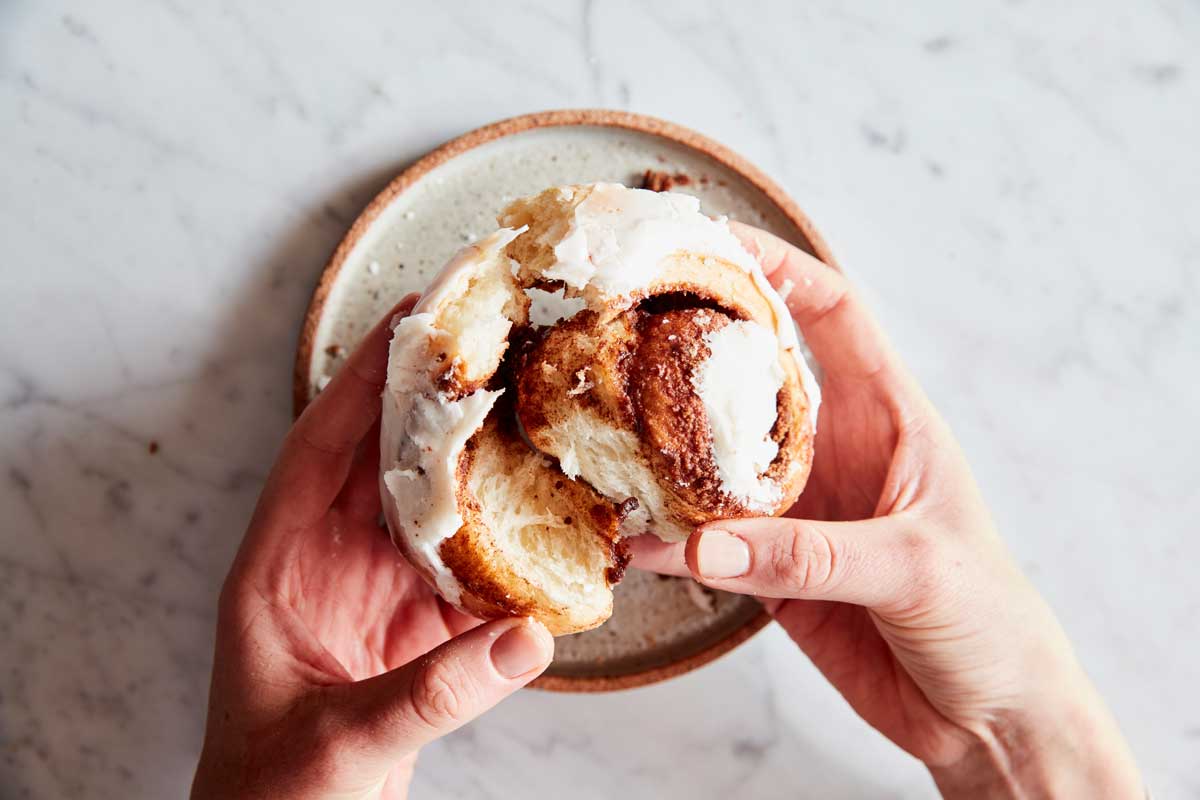 Hands pulling apart baked cinnamon rolls