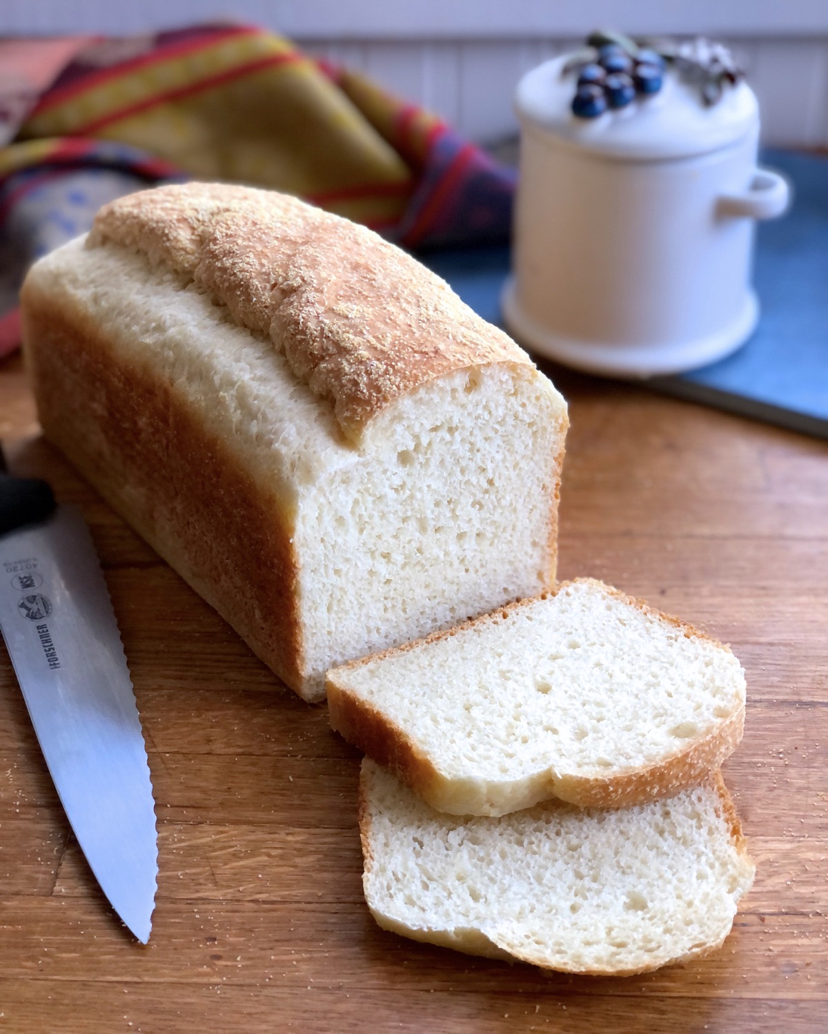 Loaf of sourdough bread, several slices cut, knife on side and jam jar behind.