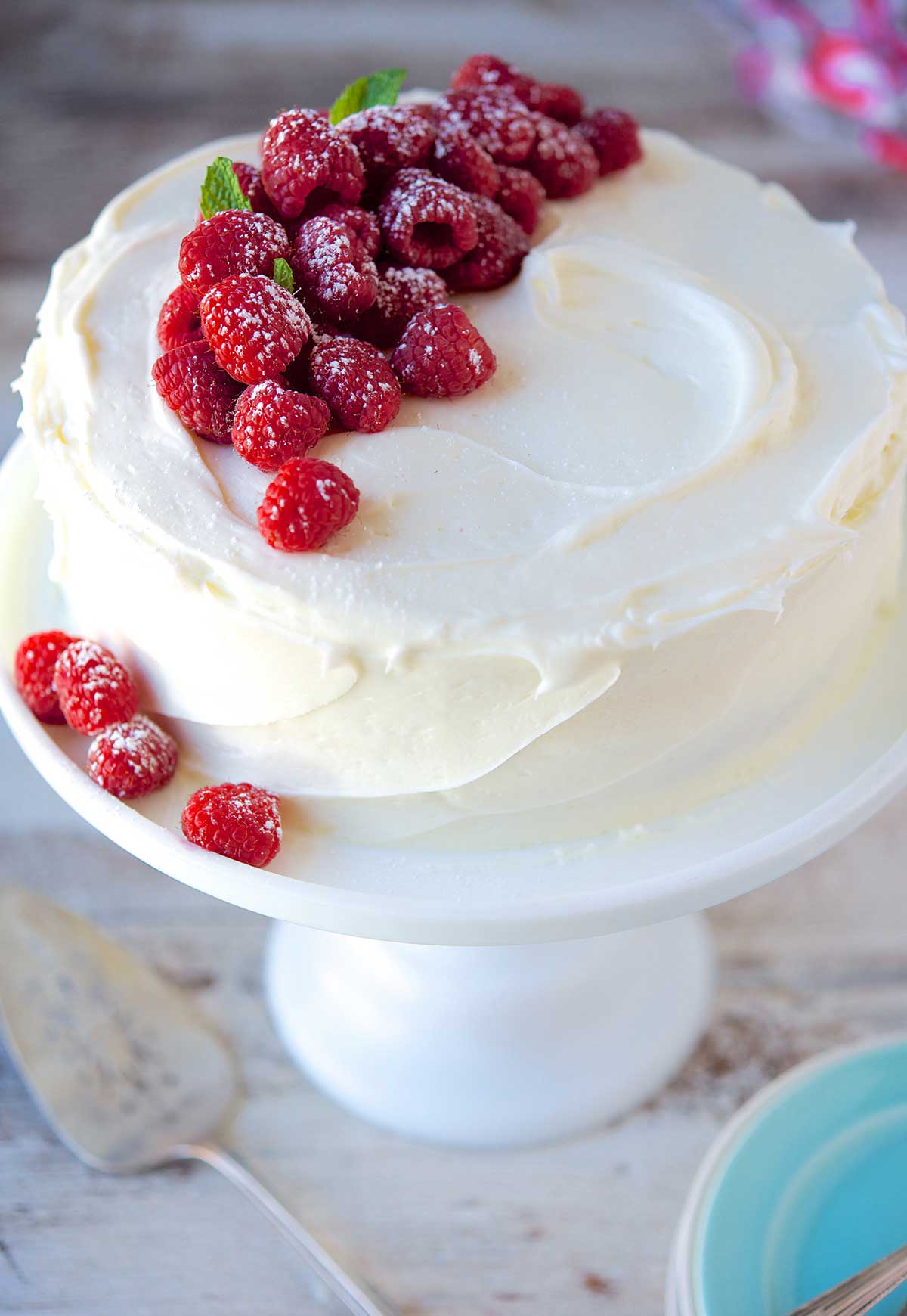 A tender white cake covered in buttercream frosting and topped with fresh raspberries