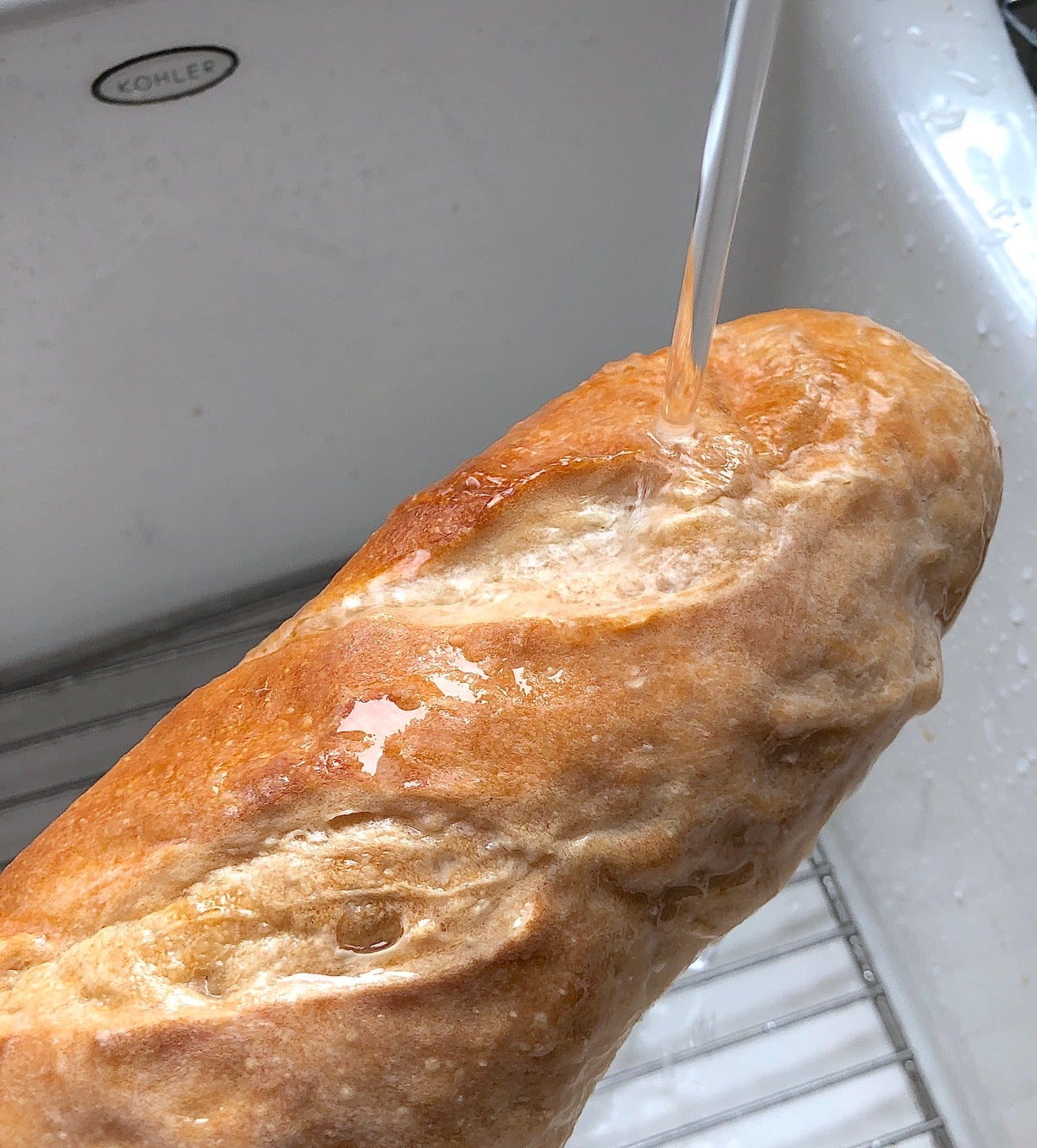 Baguette being wet under a water faucet