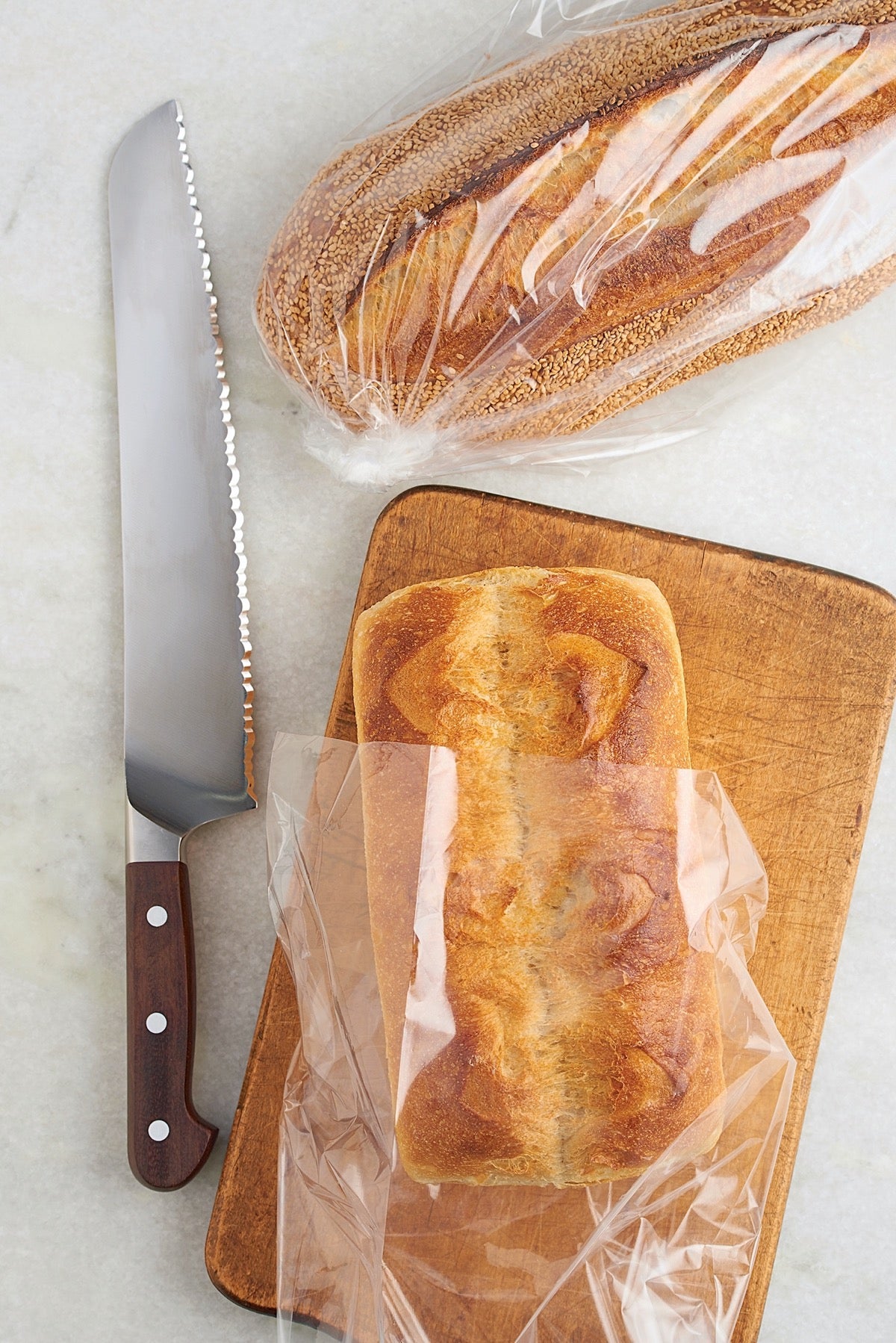 Two loaves of crusty bread in bread bags with a knife..