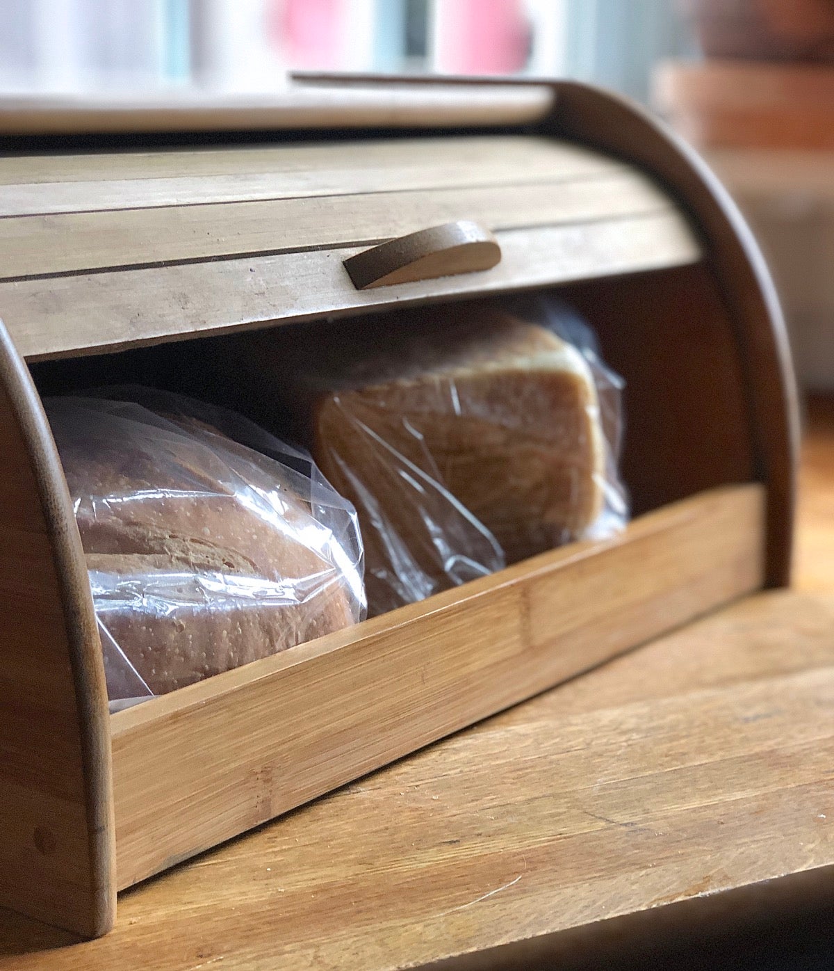 Two loaves of bread stored in a lidded wooden bread box.