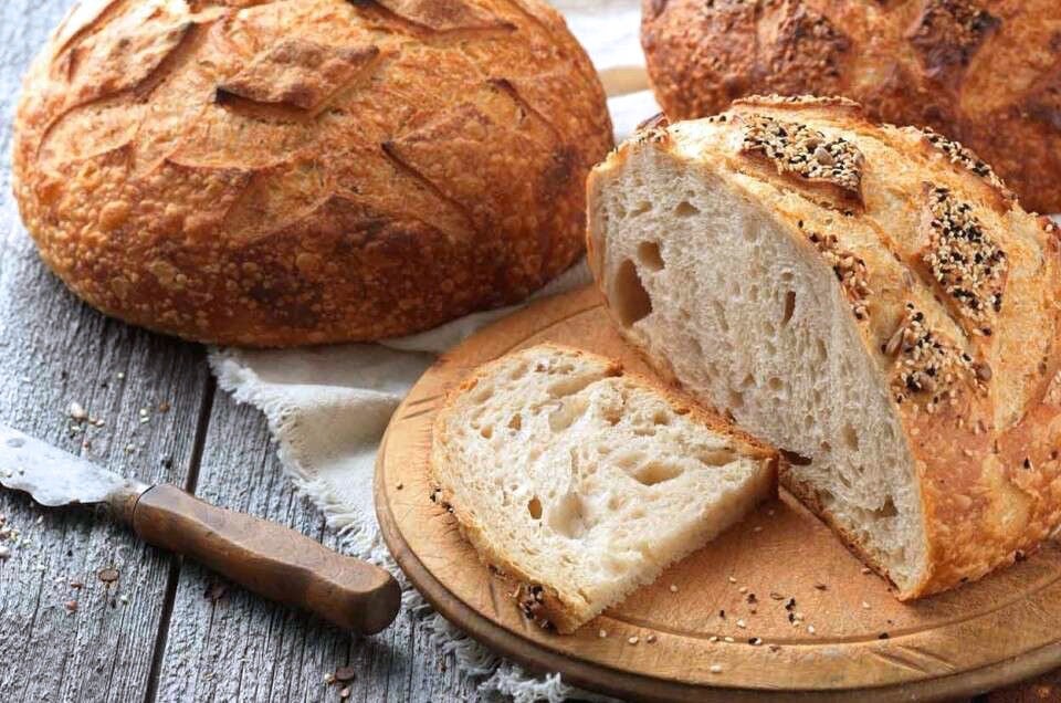 Round loaf of sourdough bread on a cutting board, sliced, two more round loaves in the background.