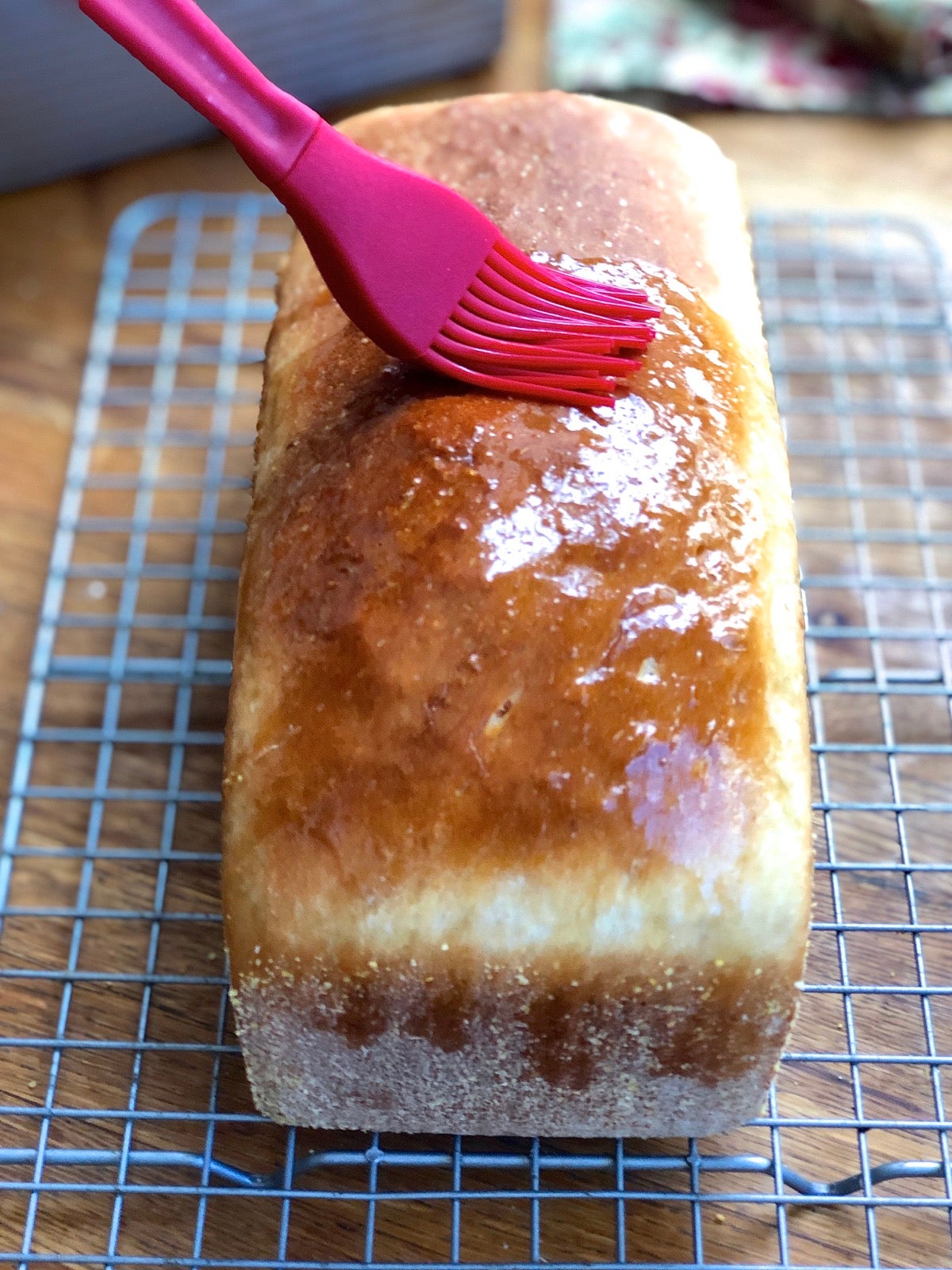 Loaf of bread hot from the oven, its crust being brushed with melted butter.