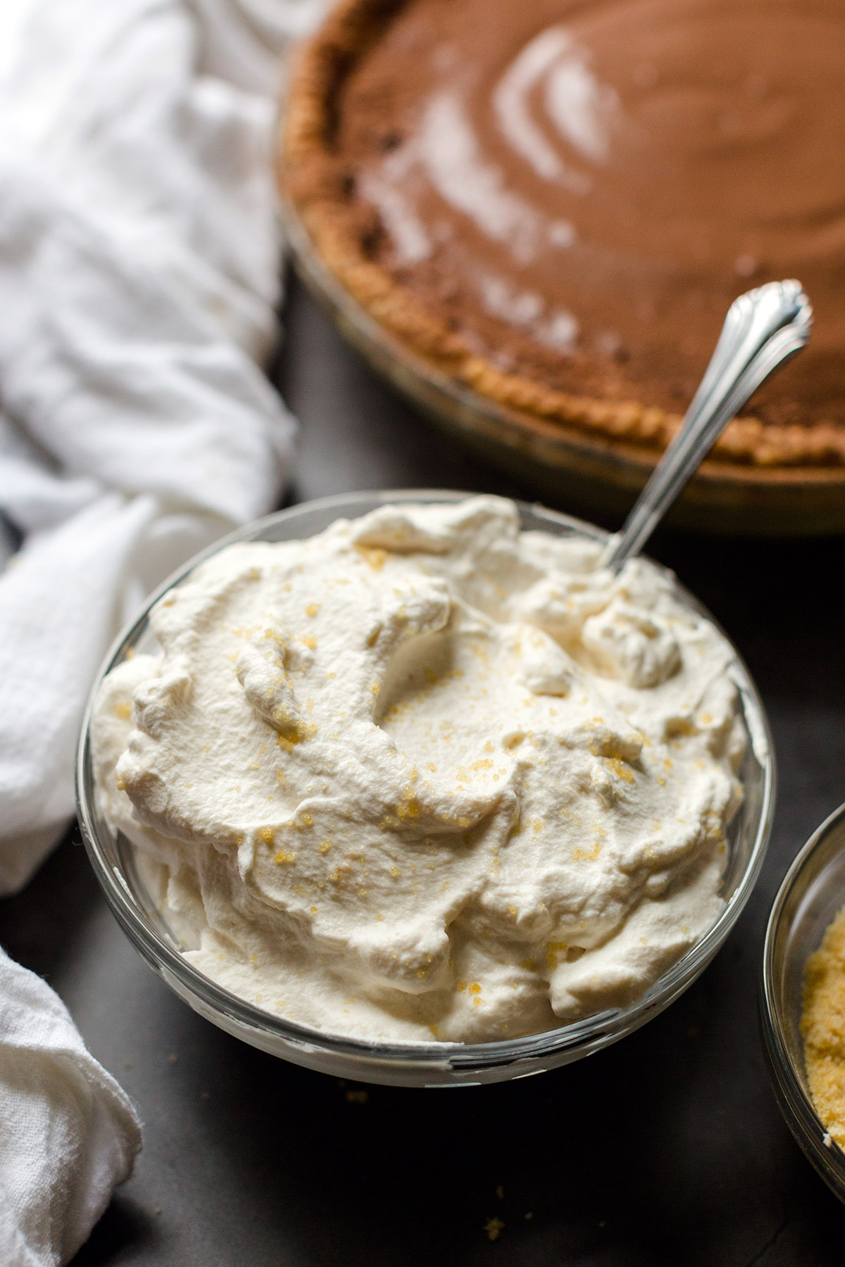A bowl of toasted sugar whipped cream with a chocolate cream pie in the background