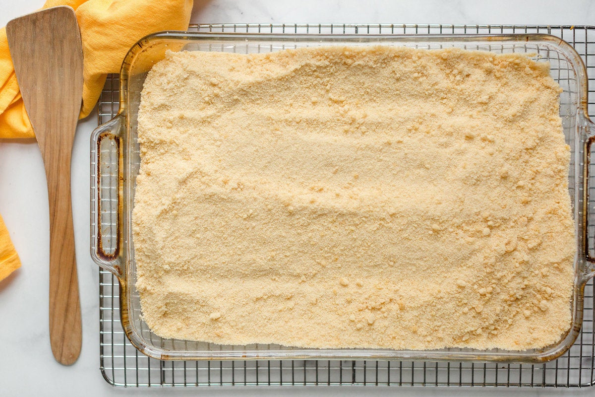 A glass pan of toasted sugar on a cooling rack with a linen and stirrer