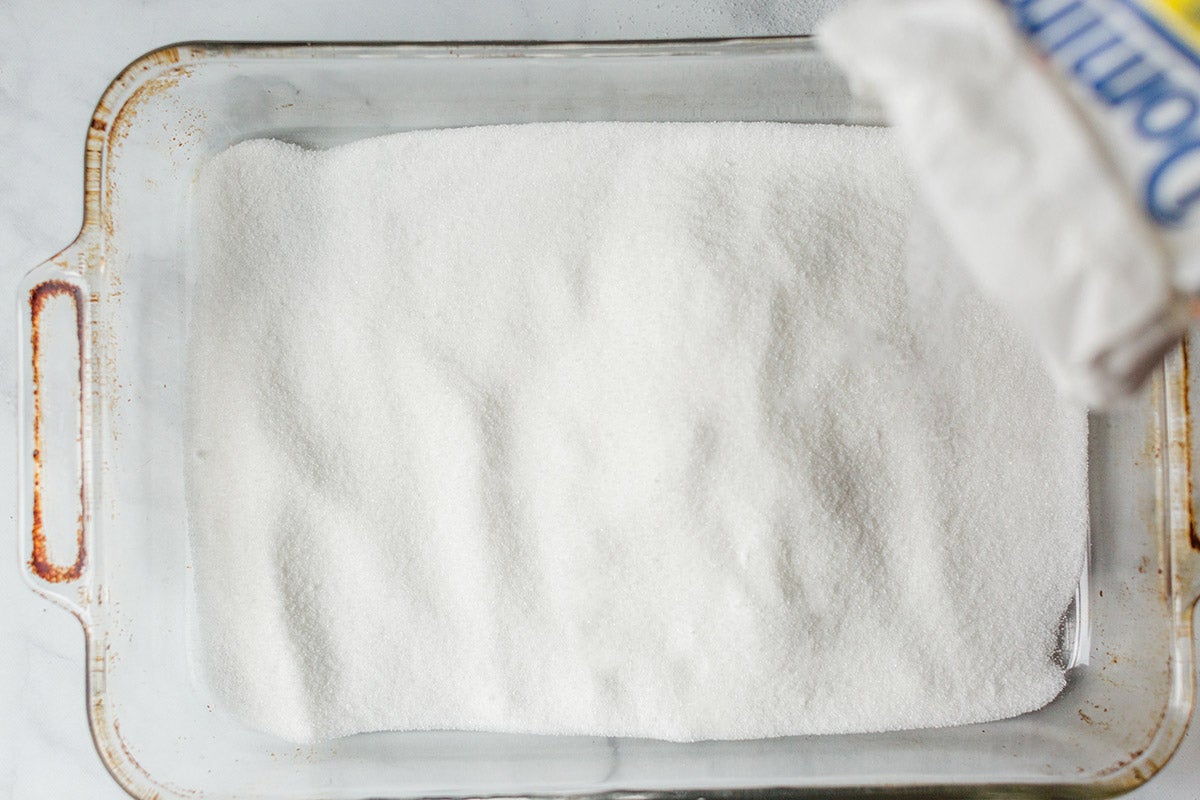 A baker pouring granulated white sugar into a 9" by 13" pan to toast it